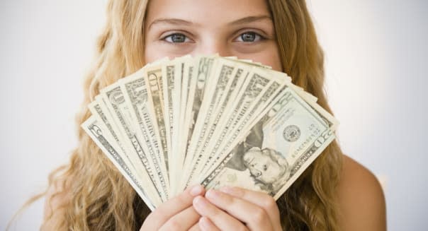 Girl (12-13) holding money fan against her face