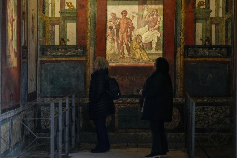 People admire frescoes in a "triclinium", or dining room, called " Hall of Ixium", part of the Ancient Roman Domus Vettiorum, House of Vettii, in the Pompeii Archeological Park, near Naples, southern Italy, Wednesday, Dec. 14, 2022. One of Pompeii's most famous and richest domus, which contains exceptional works of art and tells the story of the social ascent of two former slaves, is opening its doors to visitors Wednesday, Jan. 11, 2023 after 20 years of restoration. (AP Photo/Andrew Medichini)