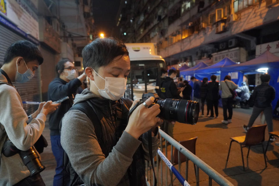 Mike Hui, foreground, takes photos of residents lining up at the temporary testing center for COVID-19, inside the lockdown area in Hong Kong on Feb. 2, 2021. Until early April, Hui was a photojournalist for the Apple Daily, a pro-democracy newspaper that shut down following the arrest of five top editors and executives and the freezing of its assets under a national security law that China's ruling Communist Party imposed on Hong Kong as part of the crackdown. (AP Photo/Kin Cheung)