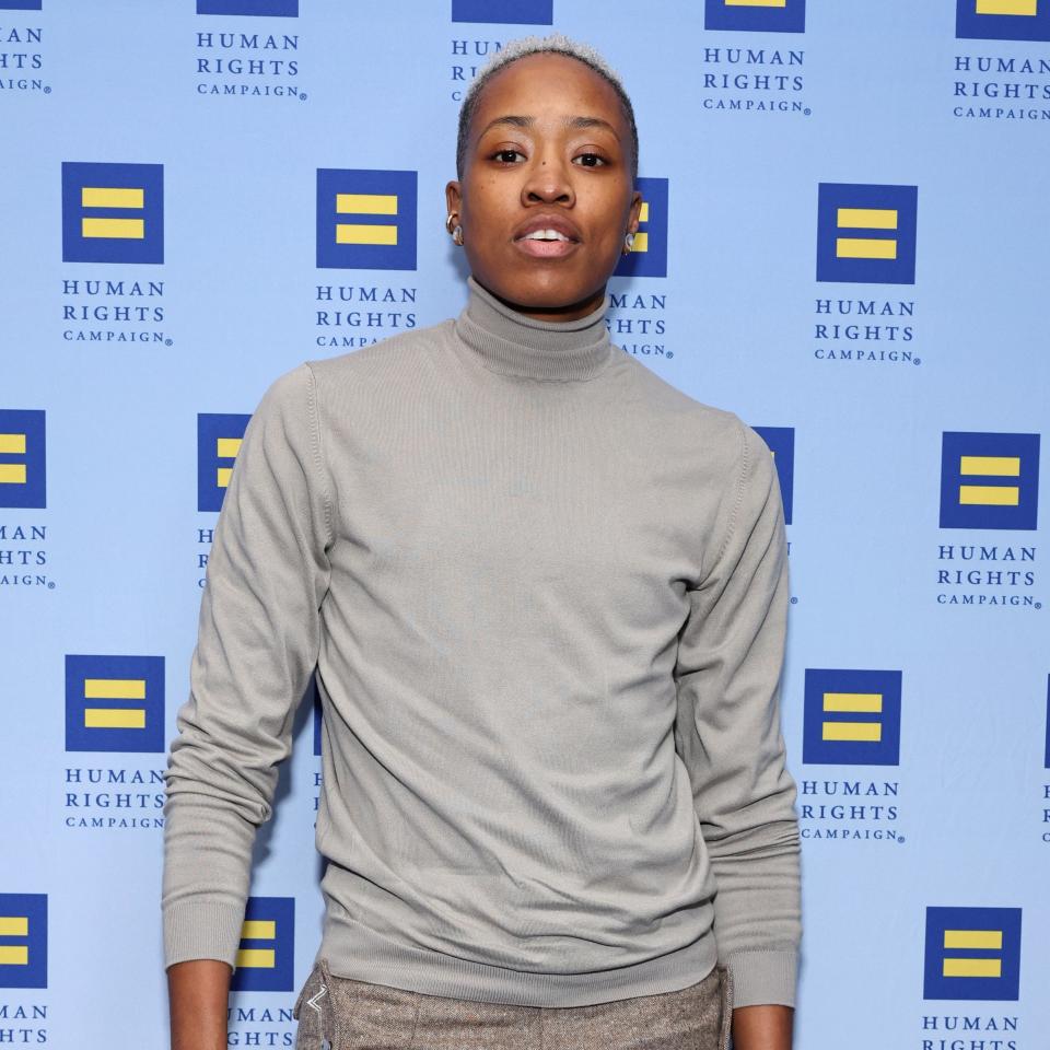 Mal in turtleneck and trousers standing in front of a Human Rights Campaign backdrop