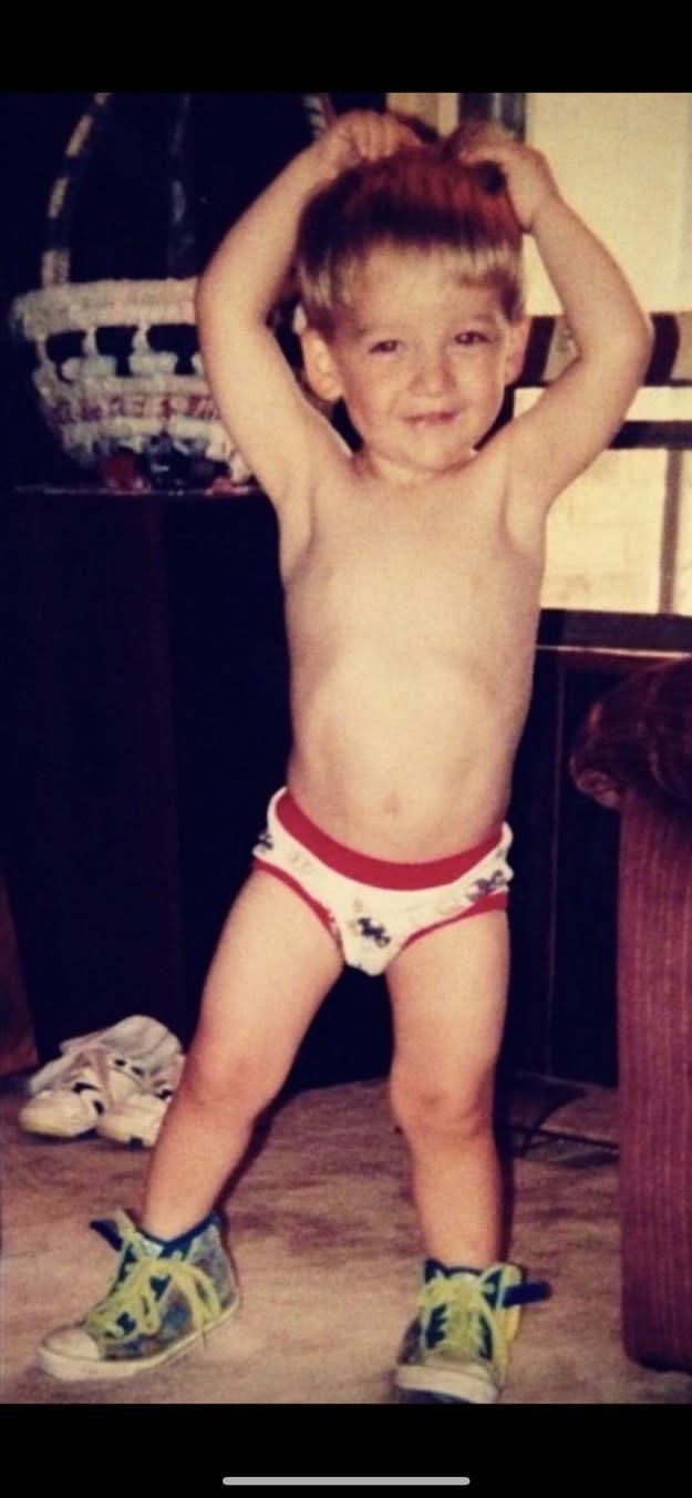 A toddler wearing sneakers and briefs with their hands over their head