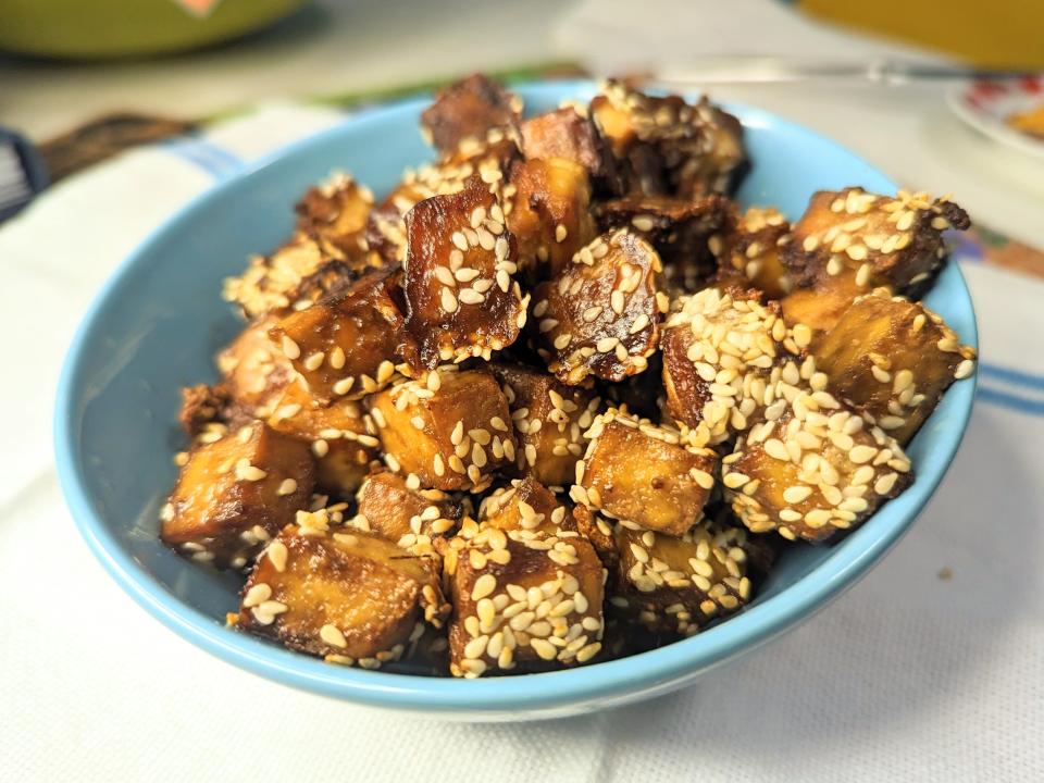 blue bowl full of crispy air fried tofu squared covered in sesame seeds