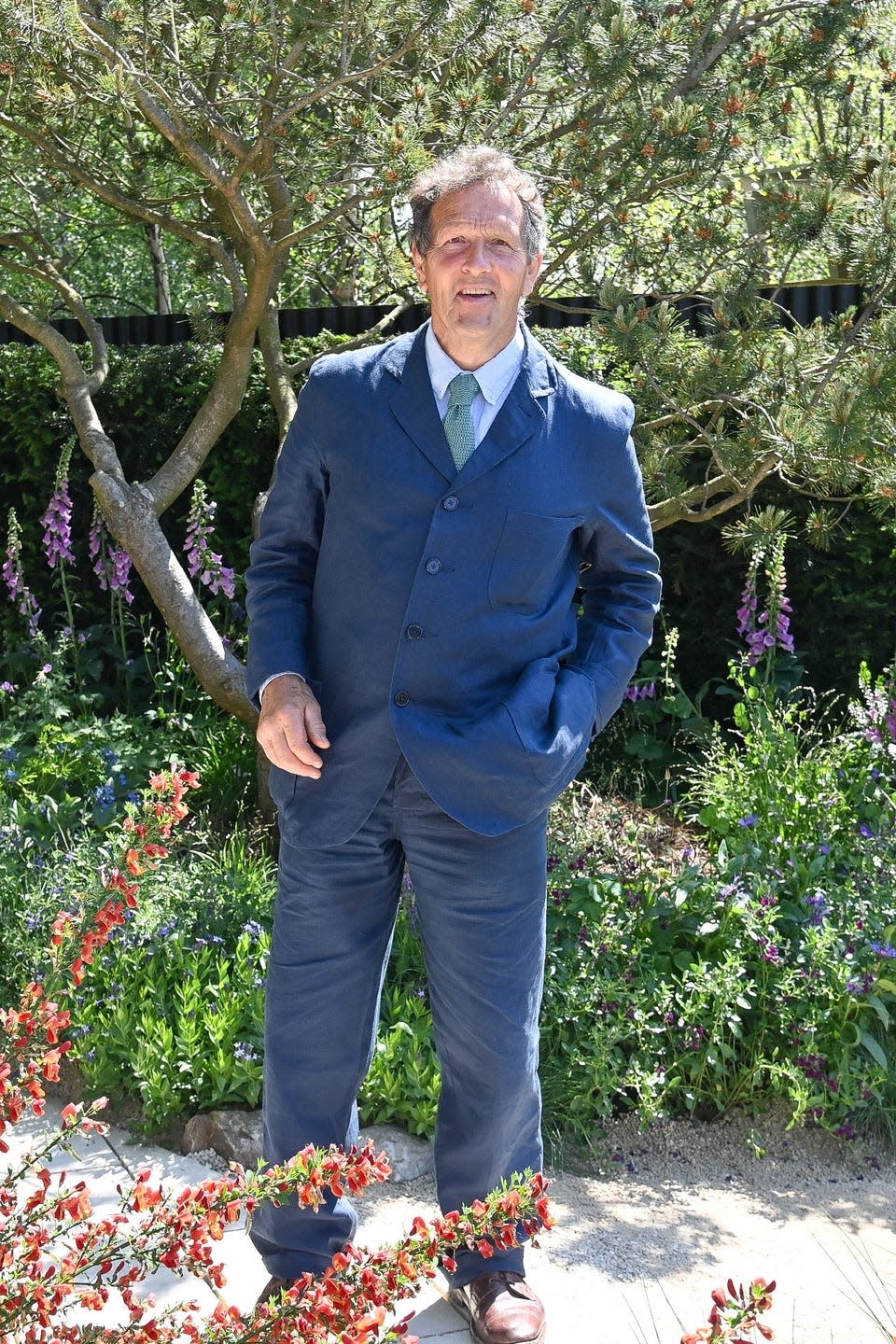 monty don at the chelsea flower show standing in front of trees and flowers