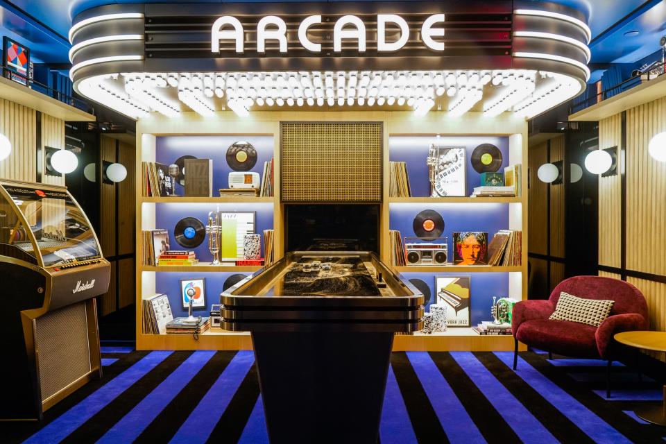 Inside a dark arcade with white bulb lights above games on a blue and black striped carpet