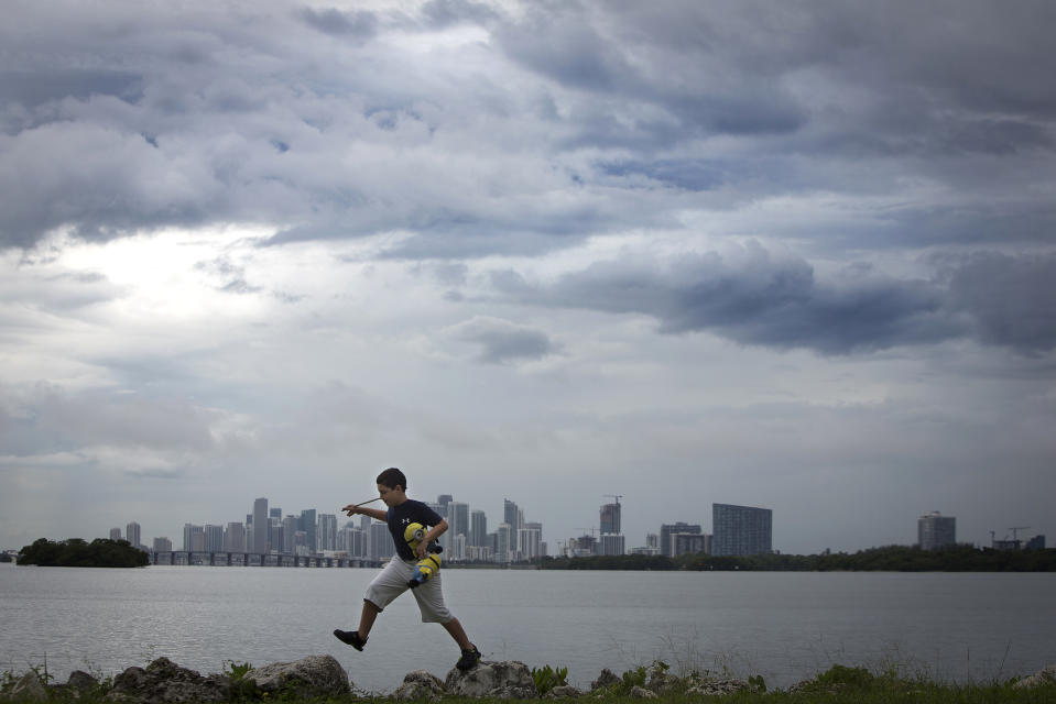 A boy jumps on rocks as he plays along a causeway on a rainy day with the city skyline in background in Miami, July 21, 2014.  REUTERS/Carlo Allegri (UNITED STATES - Tags: SOCIETY CITYSCAPE)