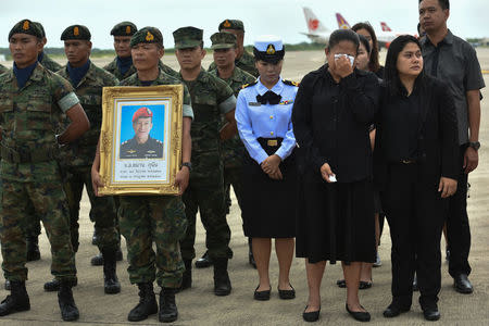 An honour guard hold up a picture of Samarn Kunan, 38, a former member of Thailand's elite navy SEAL unit who died working to save 12 boys and their soccer coach trapped inside a flooded cave, as family members weep at an airport in Rayong province, Thailand, July 6, 2018. REUTERS/Panumas Sanguanwong