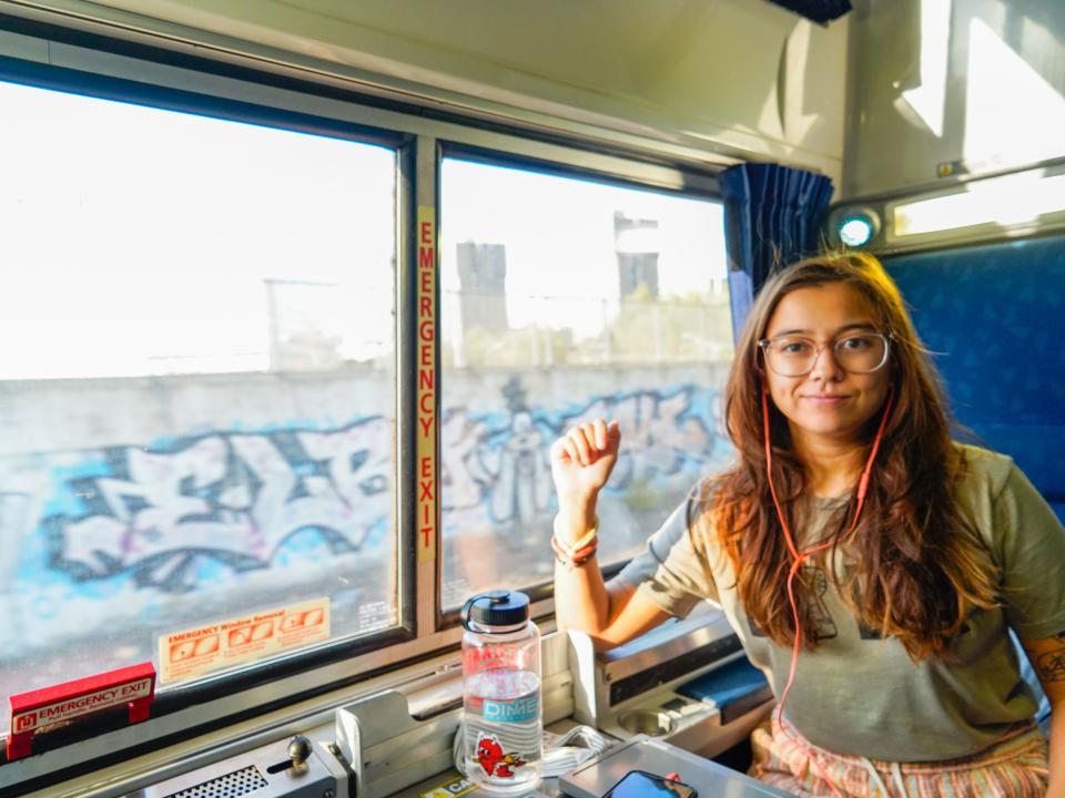 The author sits in a train car with graffiti out the window on the left