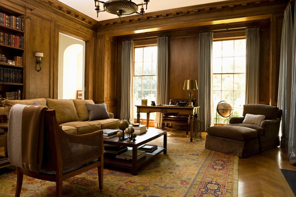 A Doric cornice wraps the walnut-paneled library, which includes an Empire chandelier from Marvin Alexander, a bronze candelabra from Jean de Merry, and a Louis XVI desk. The bookcase, flanked by Greek Ionic pilasters, opens to a hidden bar.