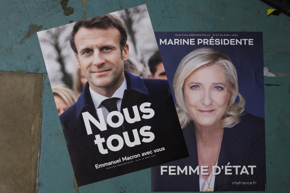 Two campaign posters, one for Macron, saying Nous tous (All of us) and Emmanuel Macron avec vous (Emmanuel Macron with you) and for Le Pen, saying Marine Présidente, Femme d'Etat, or Marine, President, Stateswoman.