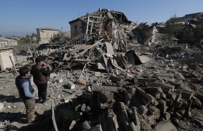 Men look at the ruins of a house following recent shelling during a military conflict over the breakaway region of Nagorno-Karabakh, in Stepanakert