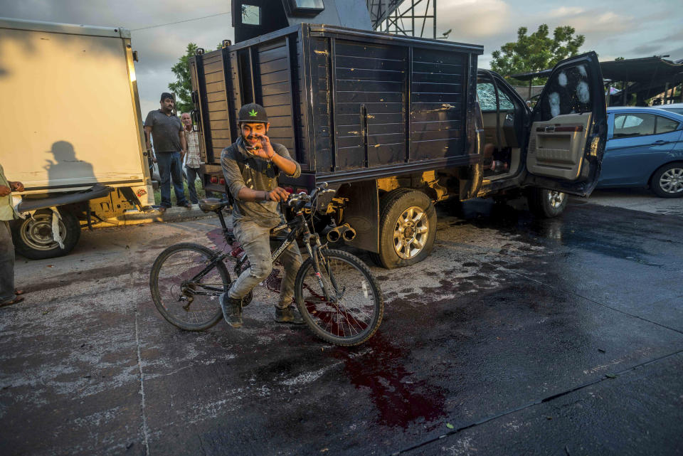 A man handles a bullet cartridge in a blooded street by a truck with a flat tire and covered with bullet hits after a gunfight in Culiacan, Mexico, Thursday, Oct. 17, 2019. An intense gunfight with heavy weapons and burning vehicles blocking roads raged in the capital of Mexico’s Sinaloa state Thursday after security forces located one of Joaquín “El Chapo” Guzmán’s sons who is wanted in the U.S. on drug trafficking charges. (AP Photo/Augusto Zurita)