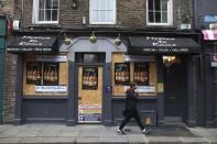 A man walks past a boarded up restaurant in Dublin, Ireland, Wednesday, Oct. 21, 2020. With COVID-19 cases on the rise, the government has imposed a tough new lockdown, shutting down non-essential shops, limiting restaurants to takeout service and ordering people to stay within five kilometers (three miles) of their homes for the next six weeks. (AP Photo/Peter Morrison)