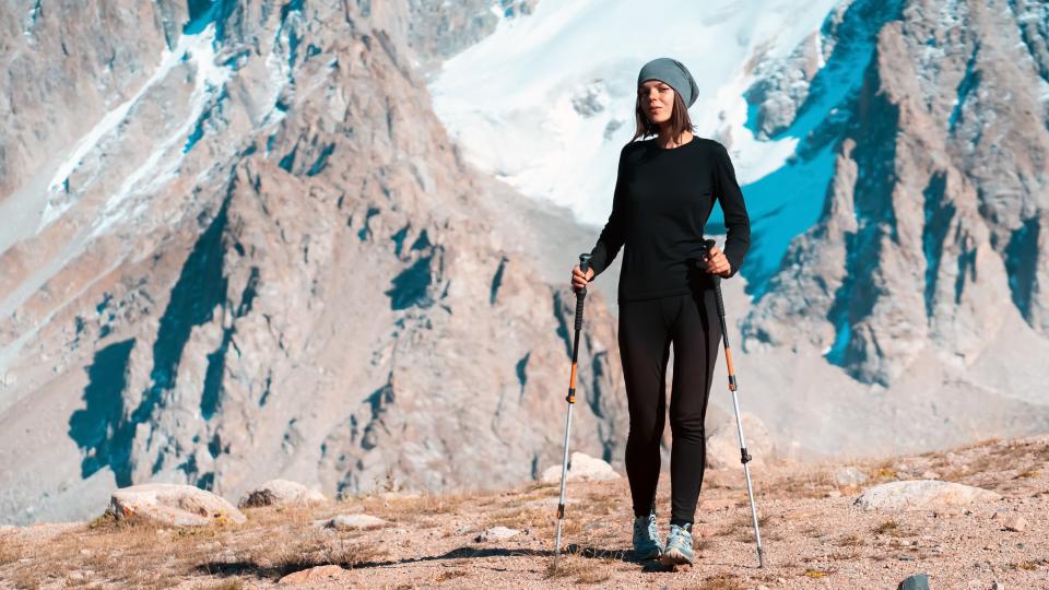 girl in thermal underwear with trekking poles walks along the trail among the snow-capped high peaks of the mountains