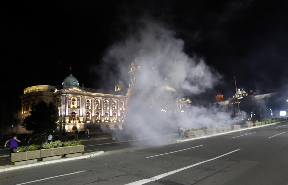 Protesters run from tear gas in front of Serbian parliament building in Belgrade, Serbia, Tuesday, July 7, 2020. Thousands of people protested the Serbian president's announcement that a lockdown will be reintroduced after the Balkan country reported its highest single-day death toll from the coronavirus Tuesday. (AP Photo/Darko Vojinovic)