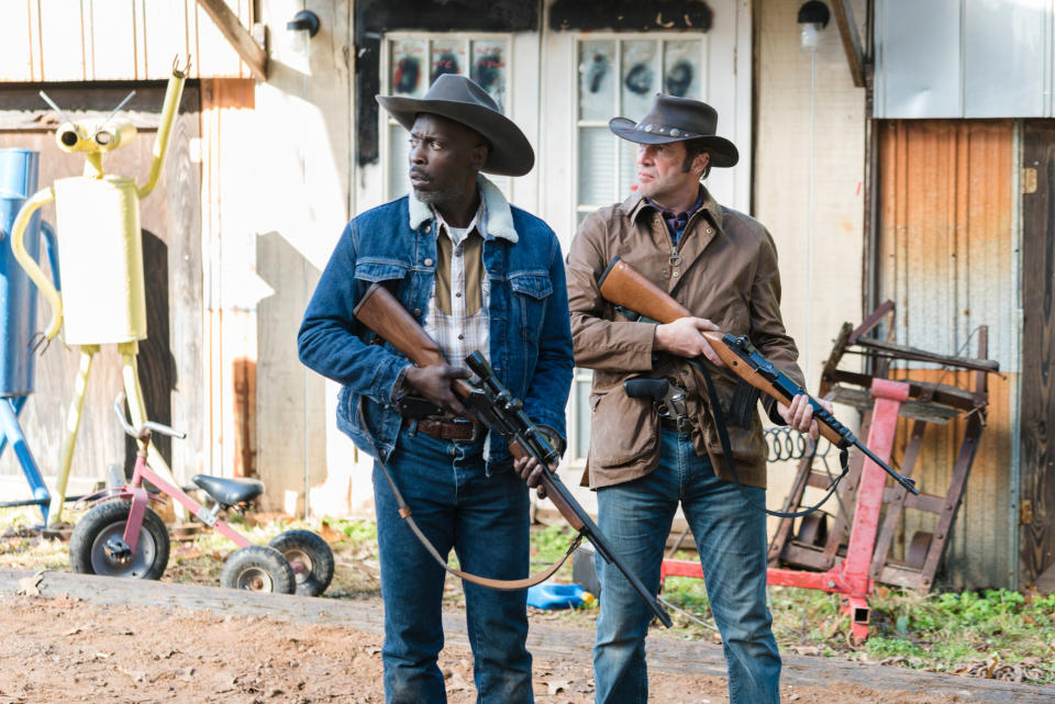 Two men walk across a farm holding guns