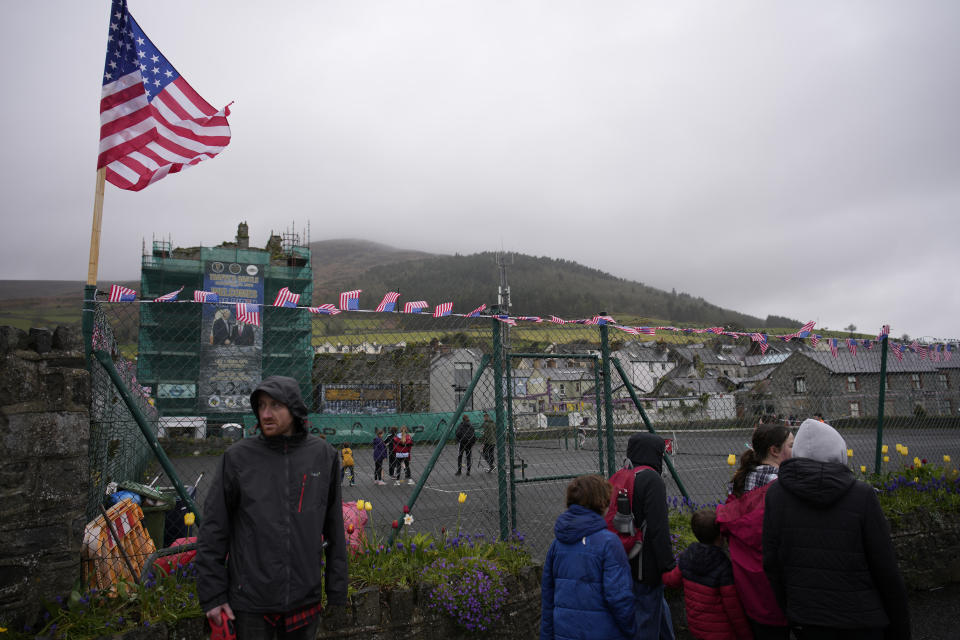 Pedestrians look at flags and bunting in Carlingford, Ireland, Tuesday, April 11, 2023, as final preparations are made for President Joe Biden's visit to the town later in the week. President Biden is visiting Northern Ireland and Ireland to celebrate the 25th Anniversary of the Good Friday Agreement. (AP Photo/Christophe Ena)