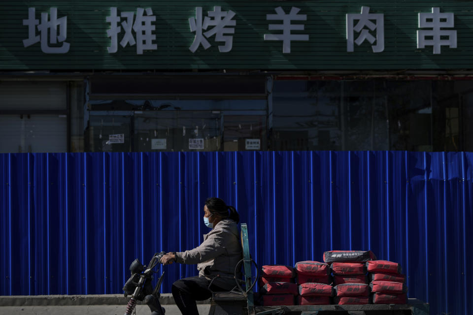 A woman wearing a face mask rides on a cart loaded with construction cements past a barricaded shuttered barbecue restaurant in Beijing on Oct. 10, 2022. A meeting of the ruling Communist Party to install leaders gives President Xi Jinping, China's most influential figure in decades, a chance to stack the ranks with allies who share his vision of intensifying pervasive control over entrepreneurs and technology development. (AP Photo/Andy Wong)