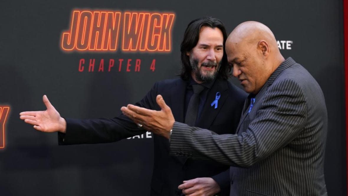 Keanu Reeves (left) and Laurence Fishburne, cast members in “John Wick: Chapter 4,” walk the carpet together at the film’s premiere Monday night at the TCL Chinese Theatre in Los Angeles. They wore blue ribbons to honor late castmate Lance Reddick. (Photo: Chris Pizzello/AP)