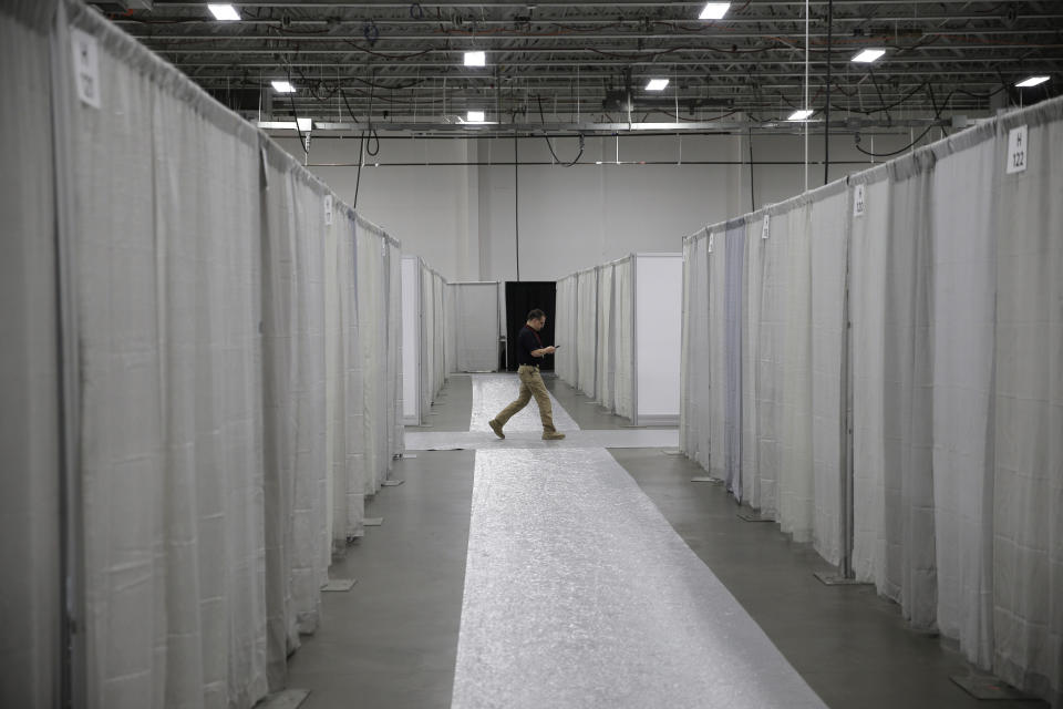 FILE- In this April 2, 2020 file photo, a man walks a corridor between rows of makeshift rooms at the nearly completed field medical station set up at the Meadowlands Exposition Center in Secaucus, N.J. The station is set up in Hudson County, one of the three hardest hit New Jersey counties by the coronavirus. (AP Photo/Seth Wenig, File)