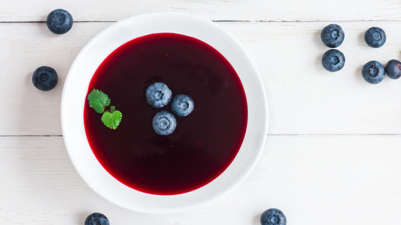 Blueberry soup in white bowl surrounded by blueberries