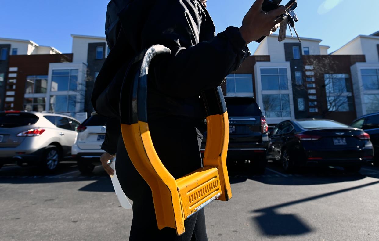 An employee of Admiral Parking Enforcement carries a boot in a paid parking lot on Monday, Feb. 19, 2024, in Nashville, Tenn. Local and officials are working on stronger regulations for the companies that boot cars. Unlike some companies that provide no grace period, Admiral Parking gives drivers 30 minutes to move their vehicles before attaching a boot to the back driver’s side wheel.