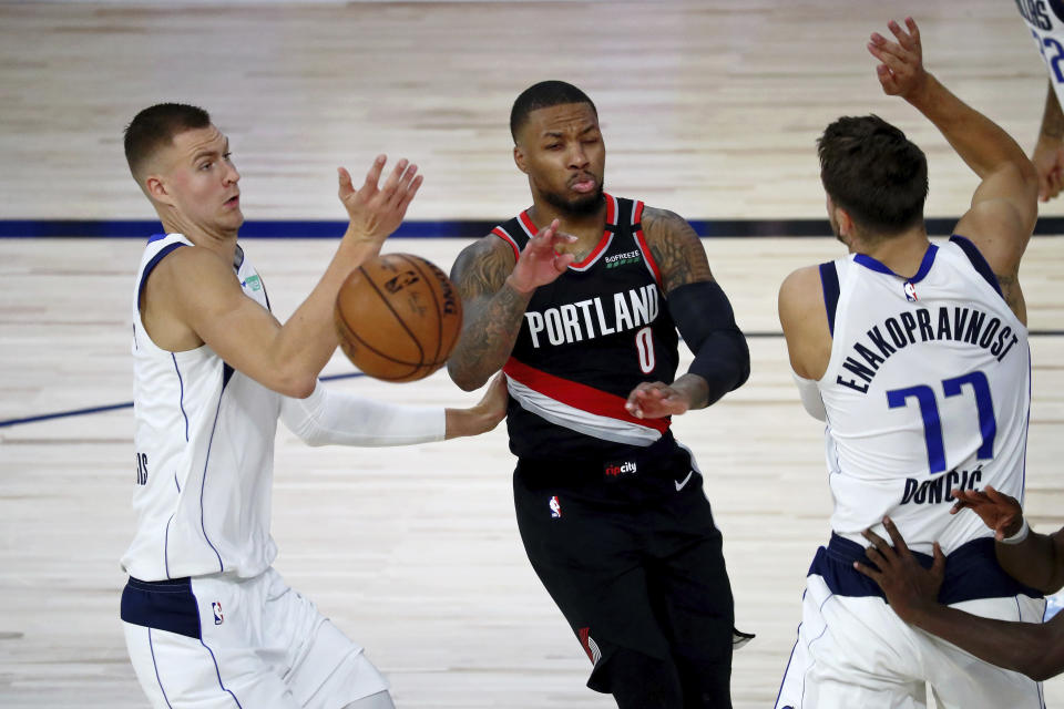 Portland Trail Blazers guard Damian Lillard (0) loses the ball while defended by Dallas Mavericks forward Kristaps Porzingis, left, and guard Luka Doncic, right, during the second half of an NBA basketball game Tuesday, Aug. 11, 2020, in Lake Buena Vista, Fla. (Kim Klement/Pool Photo via AP)