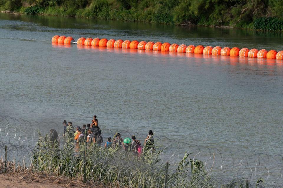 PHOTO: Migrants walk by a string of buoys placed on the water along the Rio Grande border with Mexico, July 16, 2023, in Eagle Pass, Texas. (Suzanne Cordeiro/AFP via Getty Images)