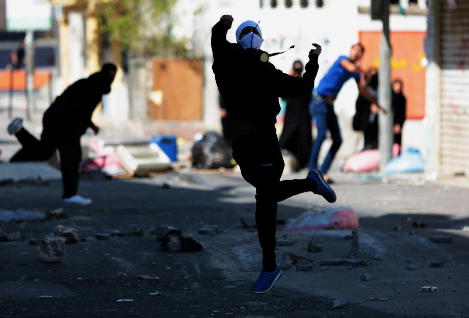 A Bahraini anti-government protester throws a stone toward riot police firing tear gas during clashes in Dih, on the edge of the capital of Manama, Bahrain, Friday, Feb. 14, 2014. An explosion rocked a bus carrying police in Bahrain on Friday, while security forces used tear gas in clashes with anti-government protesters on the third anniversary of an uprising in the small Gulf island nation. (AP Photo/Hasan Jamali)