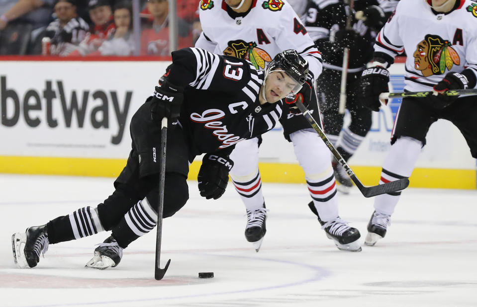 New Jersey Devils center Nico Hischier (13) reaches for the puck in front of Chicago Blackhawks defenseman Seth Jones (4) during the first period of an NHL hockey game Tuesday, Dec. 6, 2022, in Newark, N.J. (AP Photo/Noah K. Murray)