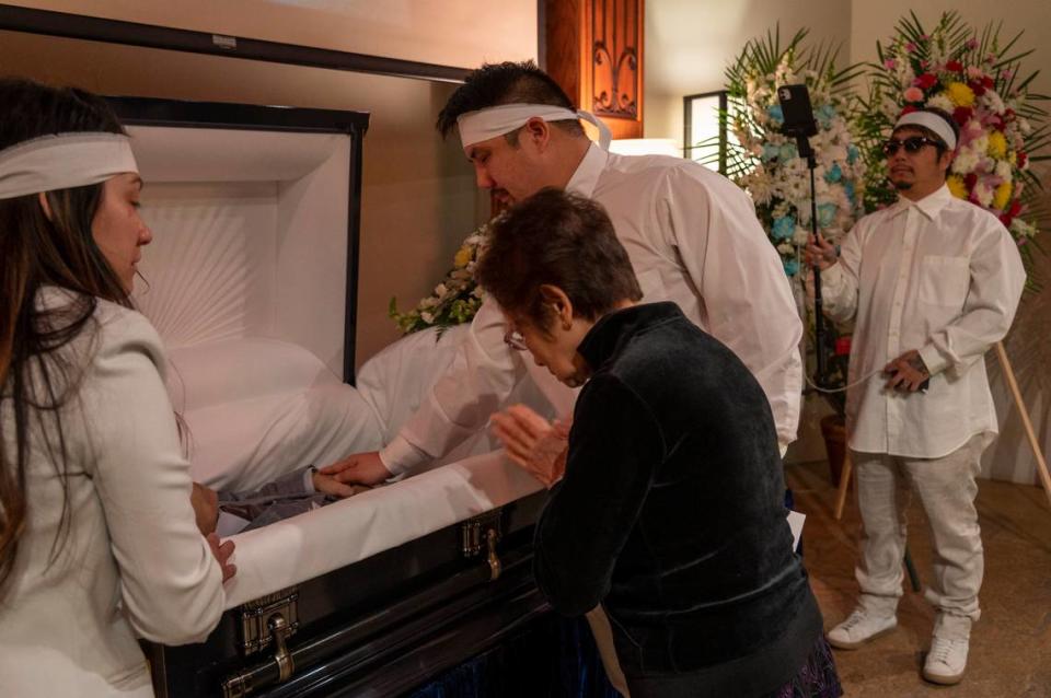 Bao Nguyen, right, records the funeral of his father Dung Tan Nguyen as his brother Michael Chambon, second from right, gives one last touch while standing alongside Trang Nguyen, left, and Kim Anh Dinh, on Wednesday, May 6, 2020, during the coronavirus outbreak. Only four family members were permitted inside the funeral chapel and the family members were torn between grieving and taking turns holding the camera to live stream the service. Other mourners sat outside or in their cars trying to view the live stream but got frustrated because the video quality was bad.