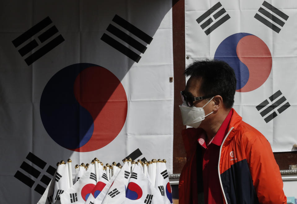 A man wearing a face mask walks near national flags displayed at a souvenir shop at the Imjingak Pavilion in Paju, South Korea, Sunday, Oct. 11, 2020. North Korean leader Kim Jong Un warned that his country would "fully mobilize" its nuclear force if threatened as he took center stage at a military parade that unveiled what appeared to be a new intercontinental ballistic missile and other weapons Saturday. (AP Photo/Lee Jin-man)