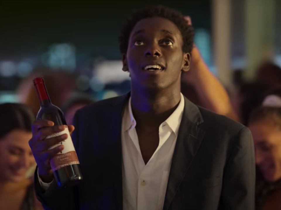 lead actor of "Zero" in a suit and carrying a bottle of wine