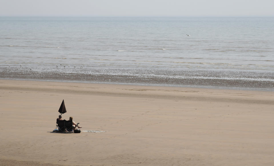 Two sunbathers sit and watch the sea on the sandy beach at Camber Sands, England, Thursday, July 25, 2019. Paris, London and places across Europe are sweltering under all-time high temperatures or near-record heat Thursday as the second heat wave this summer bakes the continent. (AP Photo/Alastair Grant)