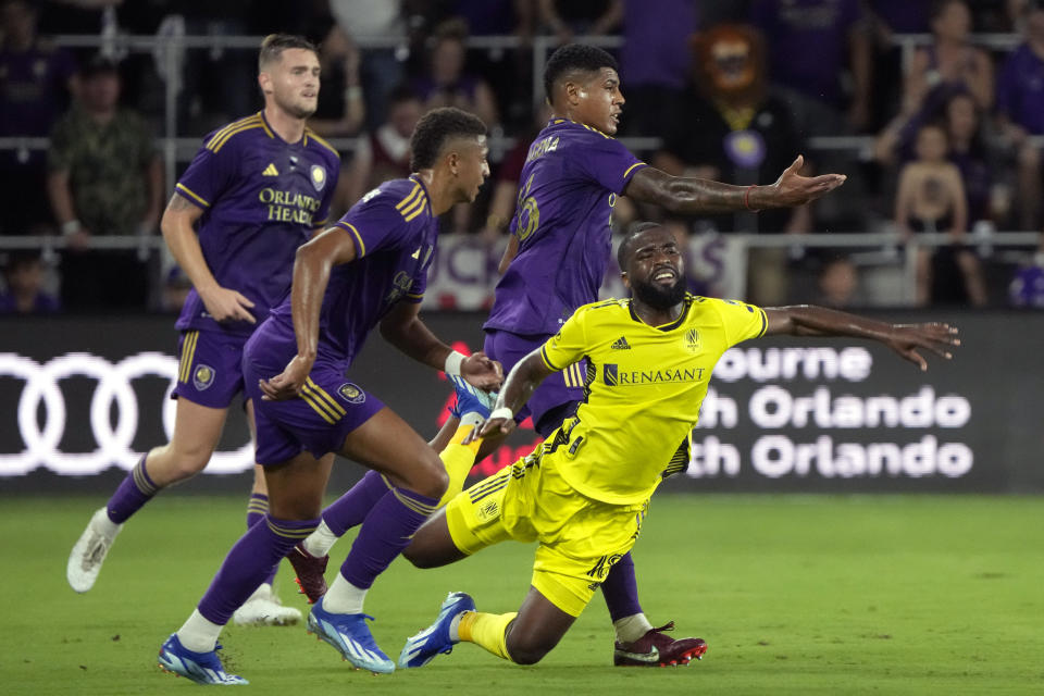 Nashville SC defender Shaq Moore, lower right, falls as he gets tripped trying to get between Orlando City defender Rafael Santos, left center, and midfielder Wilder Cartagena, right center, during the first half of an MLS playoff soccer match, Monday, Oct. 30, 2023, in Orlando, Fla. (AP Photo/John Raoux)