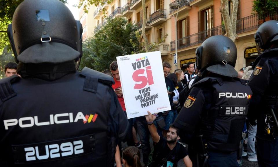 A protester holds a ‘vote yes’ placard in front of Spanish police.