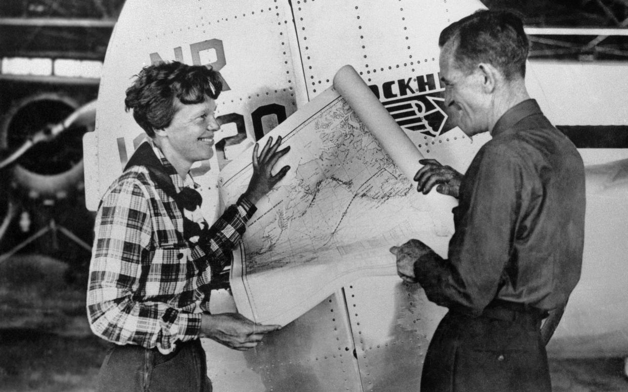 Amelia Earhart, left, and navigator Fred Noonan pose with a map of the Pacific Ocean showing the planned route of their round-the-world flight - AP