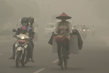 A cyclist wearing a mask rides a motorcycle as haze shrouds Cilik riwut street in Palangkaraya, October 4, 2015 in this photo taken by Antara Foto. REUTERS/Rosa Panggabean/Antara Foto