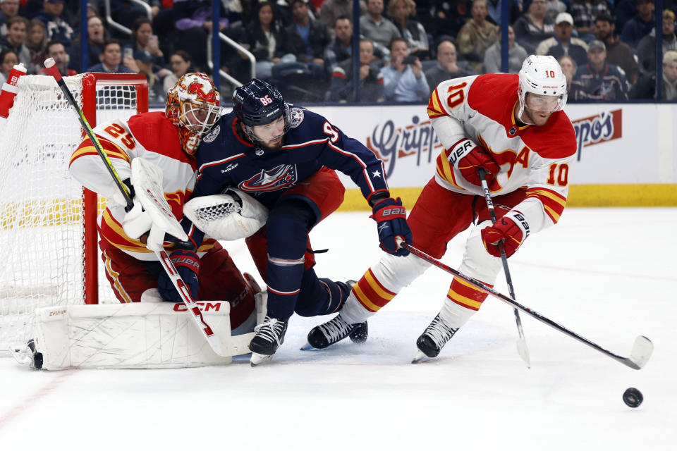 Columbus Blue Jackets forward Kirill Marchenko, center, reaches for the puck between Calgary Flames goalie Jacob Markstrom, left, and forward Jonathan Huberdeau during the second period of an NHL hockey game in Columbus, Ohio, Friday, Oct. 20, 2023. (AP Photo/Paul Vernon)