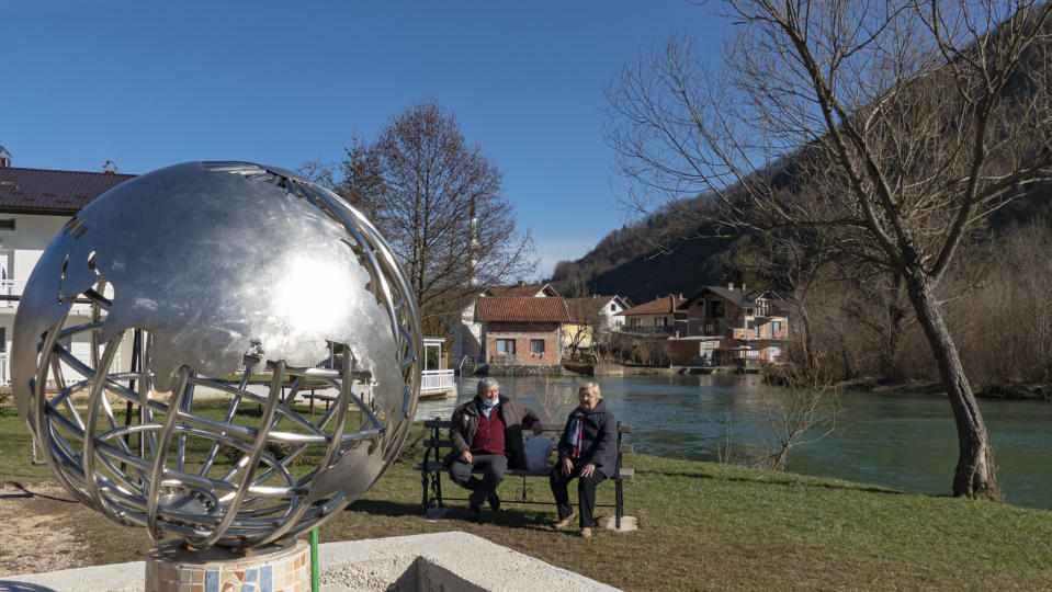 Residents sit near a metal representation of planet Earth in Jezero, Bosnia, Tuesday, Feb. 16, 2021. Bosnian villagers are setting up a video screen in the yard of the village’s sole school so people can gather to watch NASA’s Mars rover land Thursday in a crater of the Red Planet named after their small village. It will be a historic day for the 1,000 villagers, who hope that the landing of the Perseverance rover in a crater on Mars will also bring them some earthly rewards. (AP Photo/Almir Alic)