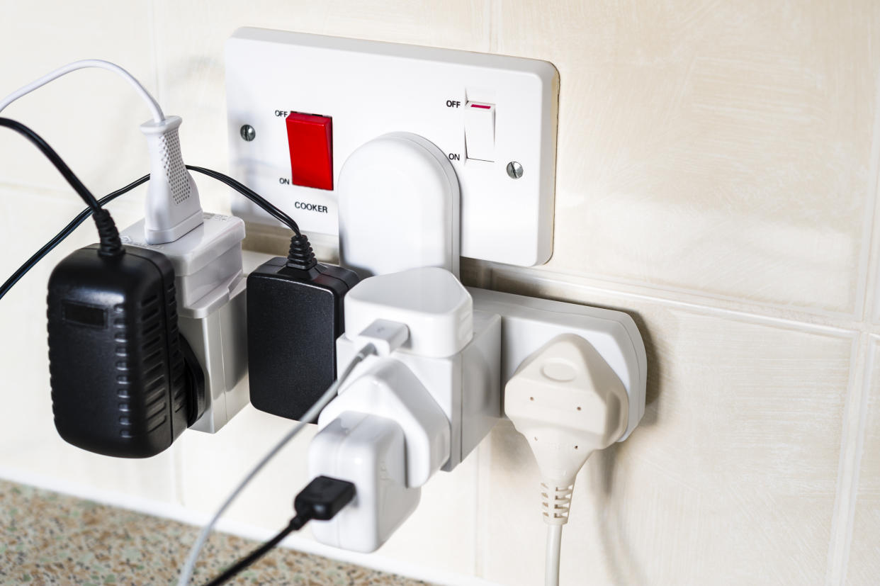 An overloaded kitchen electrical outlet, with plugs attached for mobile phone, tablet, kettle, battery charger, digital phone and electric tootbrush. UK plugs. Shallow DOF with focus on the right-hand switch.