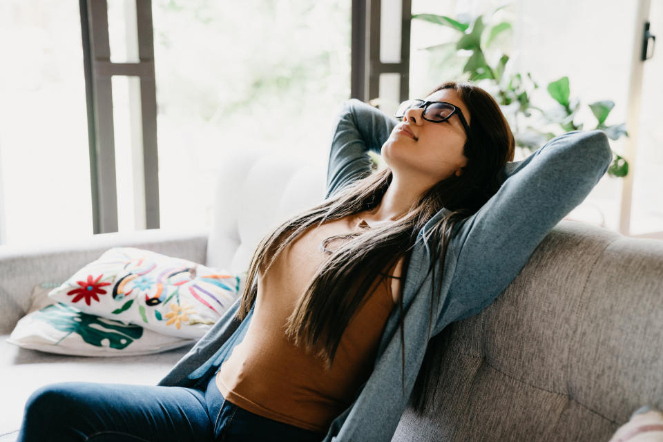 A woman relaxing on her couch with her hands behind her head