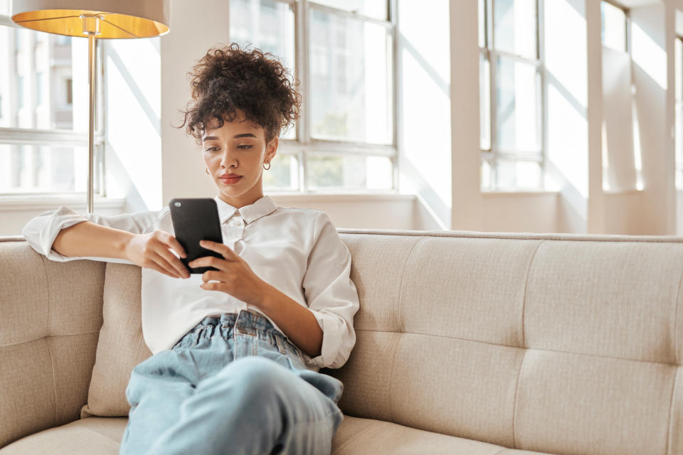 Relax, phone and woman on a sofa for social media, texting and online reading in a living room, calm and content. Black woman, smartphone and web browsing, internet and search  for entertainment