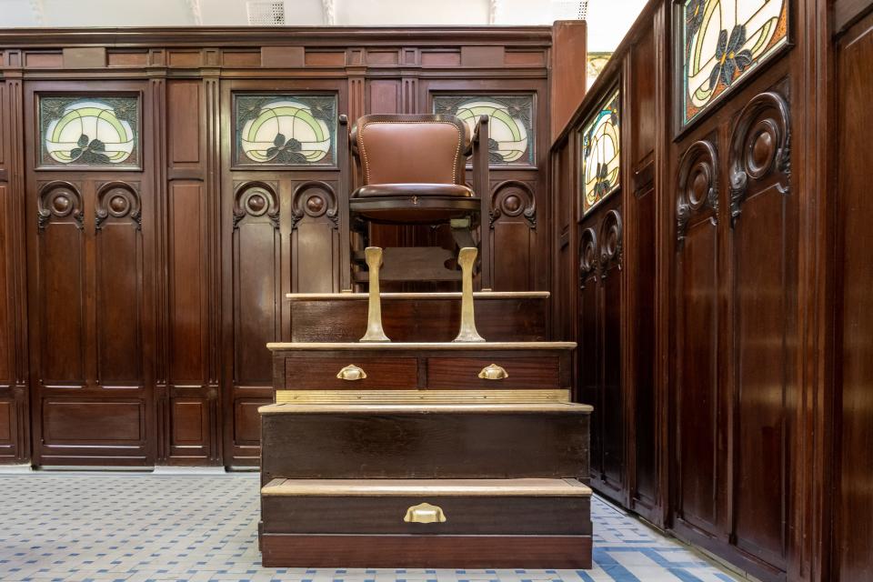 An old shoeshine chair, which is brown, sits on top of a functional miniature staircase, featuring operable drawers.