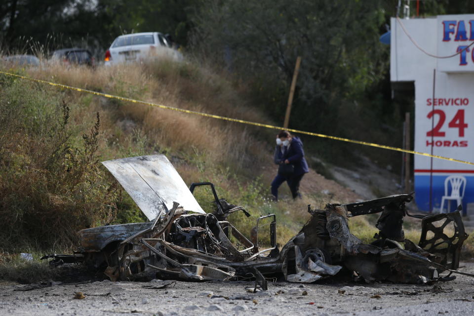 Locals walk past a burned-out car outside the Tula General Hospital, after a gang rammed several vehicles into a prison and escaped with nine inmates, in Tula, Mexico, Wednesday, Dec. 1, 2021. Local media reported that the burned-out cars found in the city after the attack were car bombs. Authorities said they were investigating how the vehicles caught fire. (AP Photo/Ginnette Riquelme)