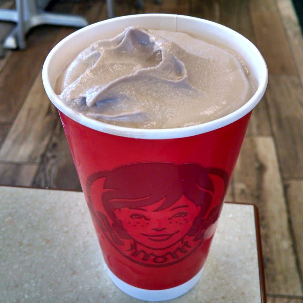 Wendy's Frosty in a paper cup without a lid on the edge of a gray table