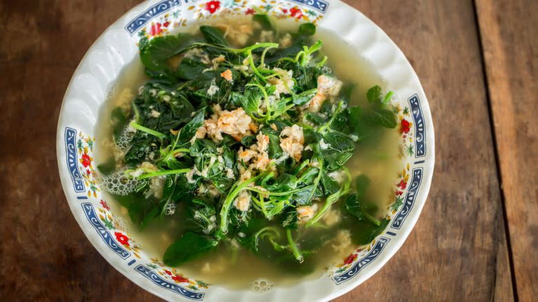 A bowl of brothy soup with leafy greens