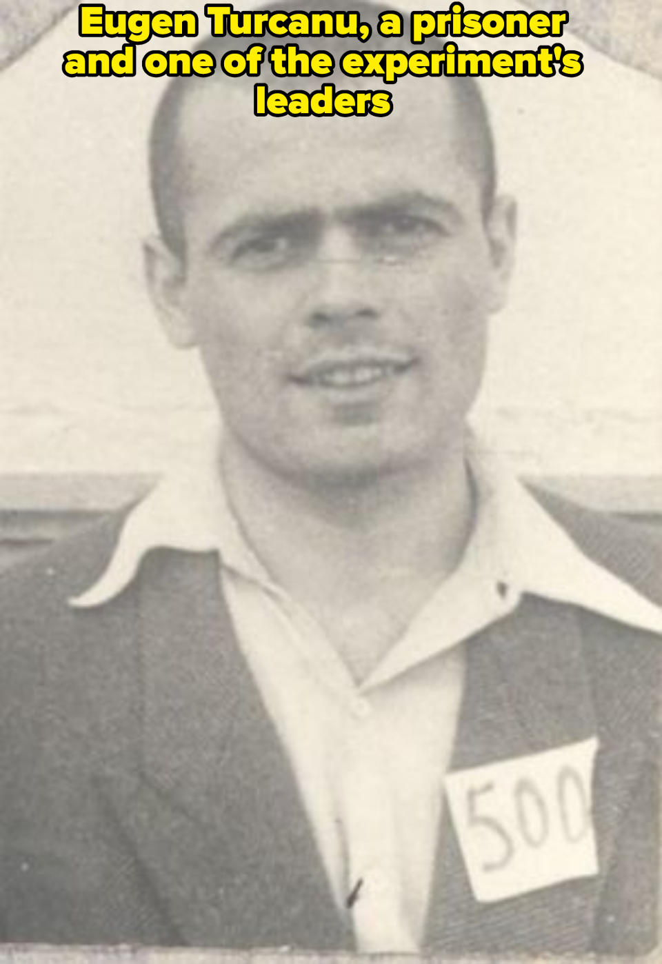 A man, wearing a collared shirt and jacket, with a tag numbered '500' pinned to his jacket