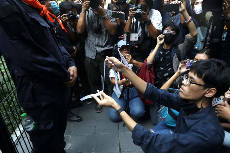 A protester makes a white ribbon as a symbol of peace in front of a police officer during anti-government protests in Bangkok