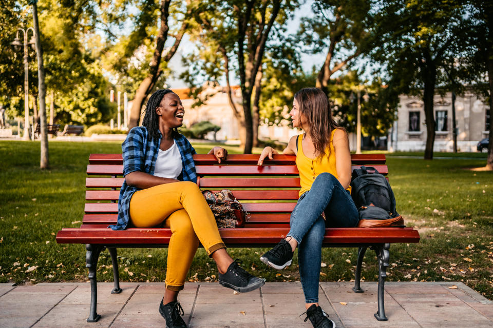 Two friends sitting on a park bench talking and laughing