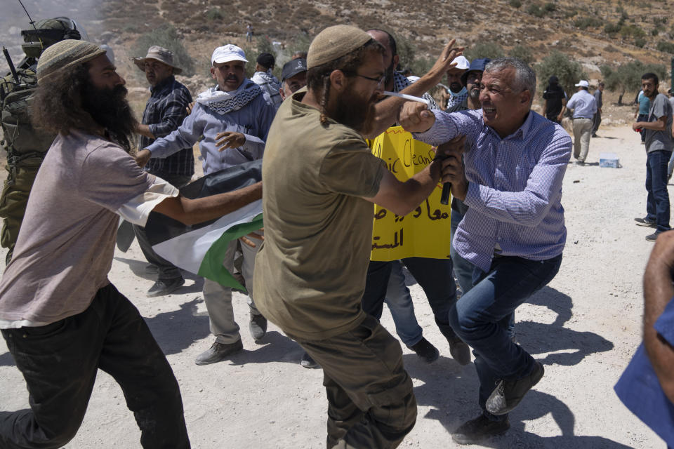 A Palestinian protester punches an Israeli settler during a scuffle between both sides while Palestinian activists blocked the street that bypasses the West Bank village of Mughayer, north of Ramallah, Friday, July 29, 2022. Palestinians protesting against Israeli settlements activities blocked a main street and scuffled with Israeli settlers and army soldiers who used teargas to disperse them. (AP Photo/Nasser Nasser)